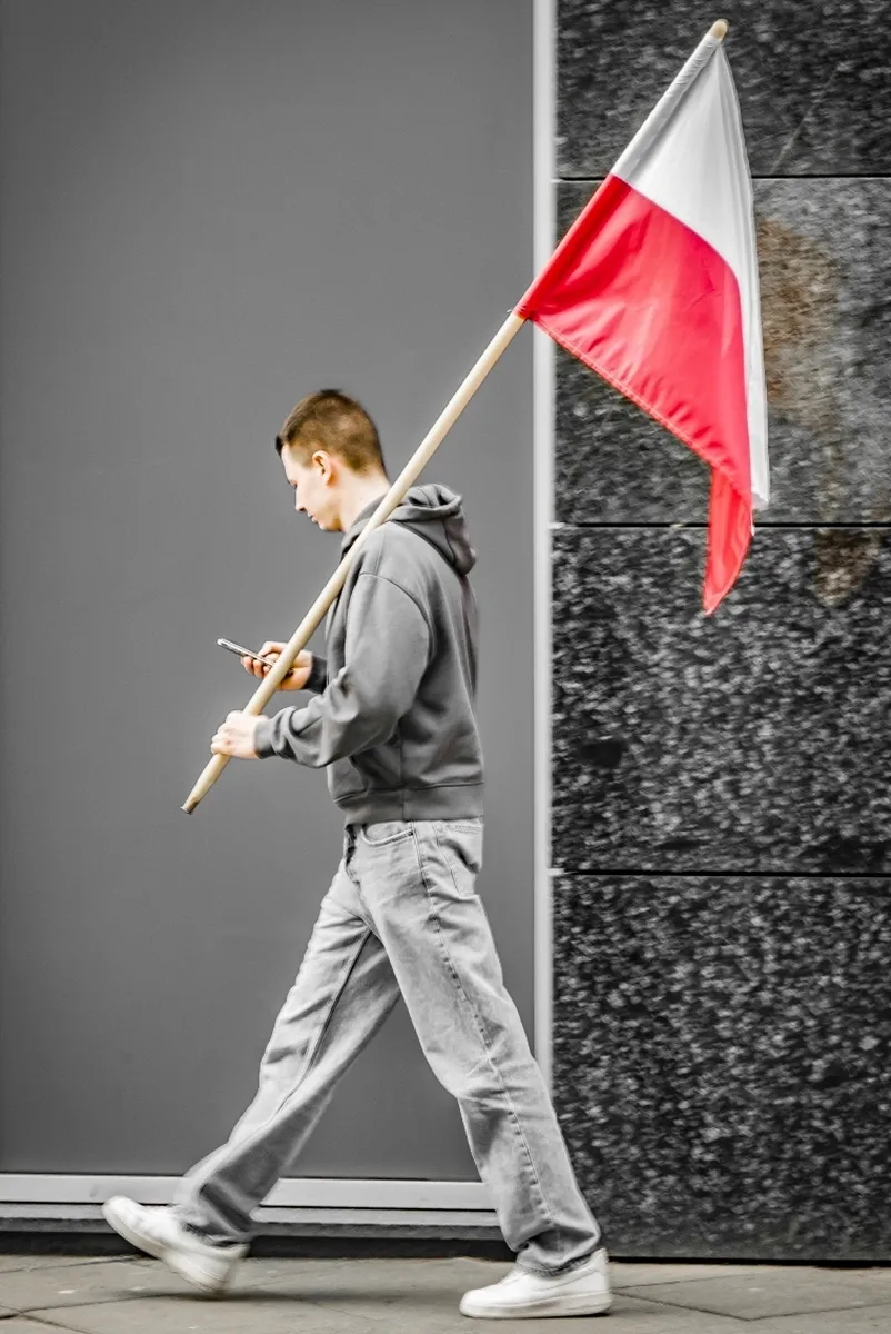 Man walking with a Polish flag while looking at his phone